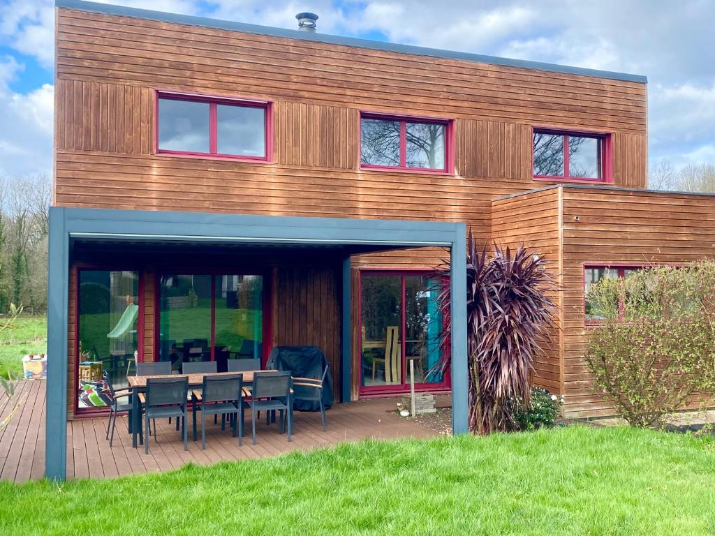 une maison en bois avec des chaises et des tables sur une terrasse dans l'établissement Maison 180m2, jardin clos, 2 terrasses, 5 mn Dinan, à Vildé-Guingalan