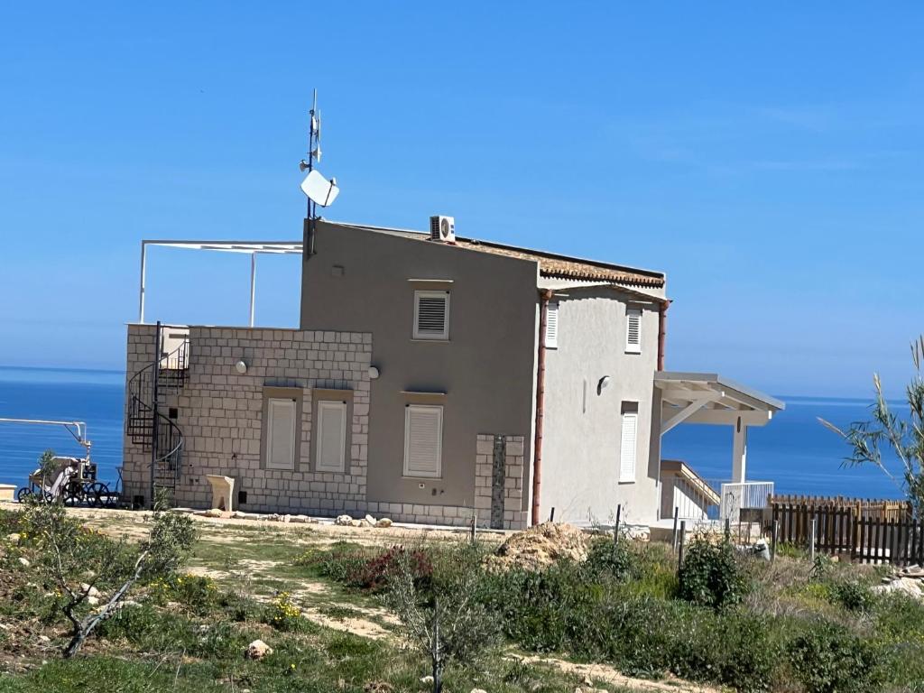 una casa su una collina con l'oceano sullo sfondo di La Finestra sul Mare dello Zingaro a Scopello