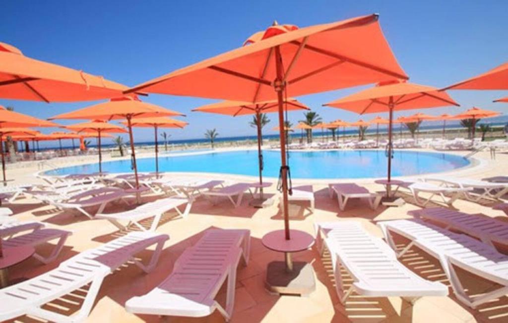 uma piscina com cadeiras brancas e guarda-sóis laranja em App S1 à l'hôtel Andalucia Beach em Bizerte