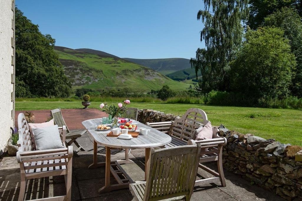 a patio with a table and chairs and a stone wall at Mossfennan House in Drummelzier