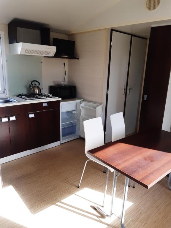 a small kitchen with a wooden table and white chairs at Mobile home S004 in Lancieux