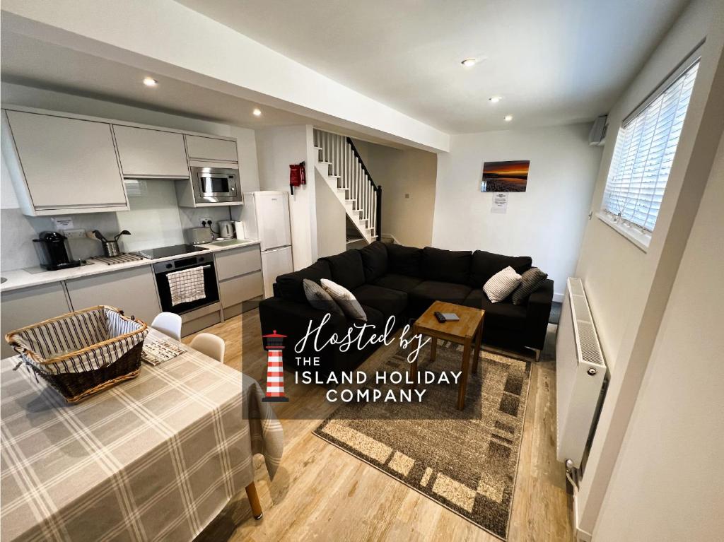 a living room with a black couch and a kitchen at Coach House Annexe in Sandown