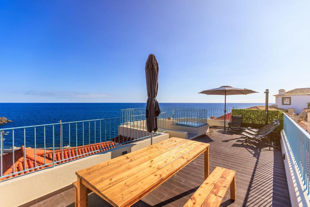 a deck with a table and an umbrella and the ocean at Villa Belafonte in Câmara de Lobos