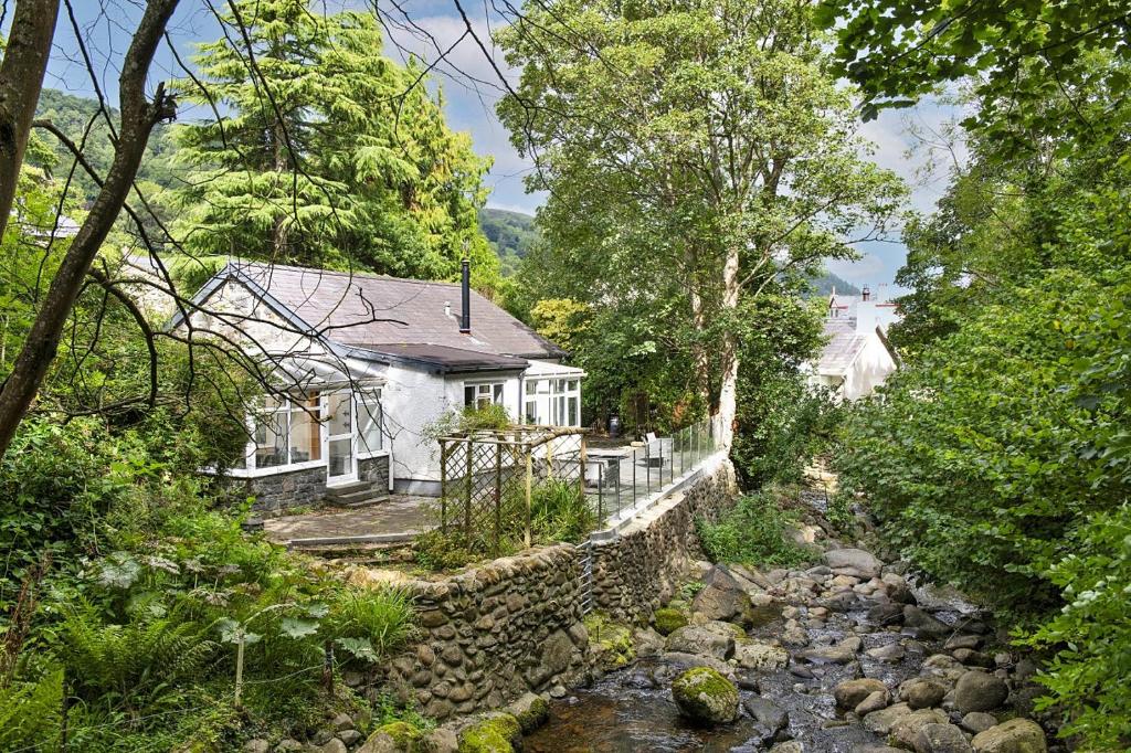 una casa blanca con una pared de piedra junto a un río en Finest Retreats - Nant Cottage, en Llangelynin
