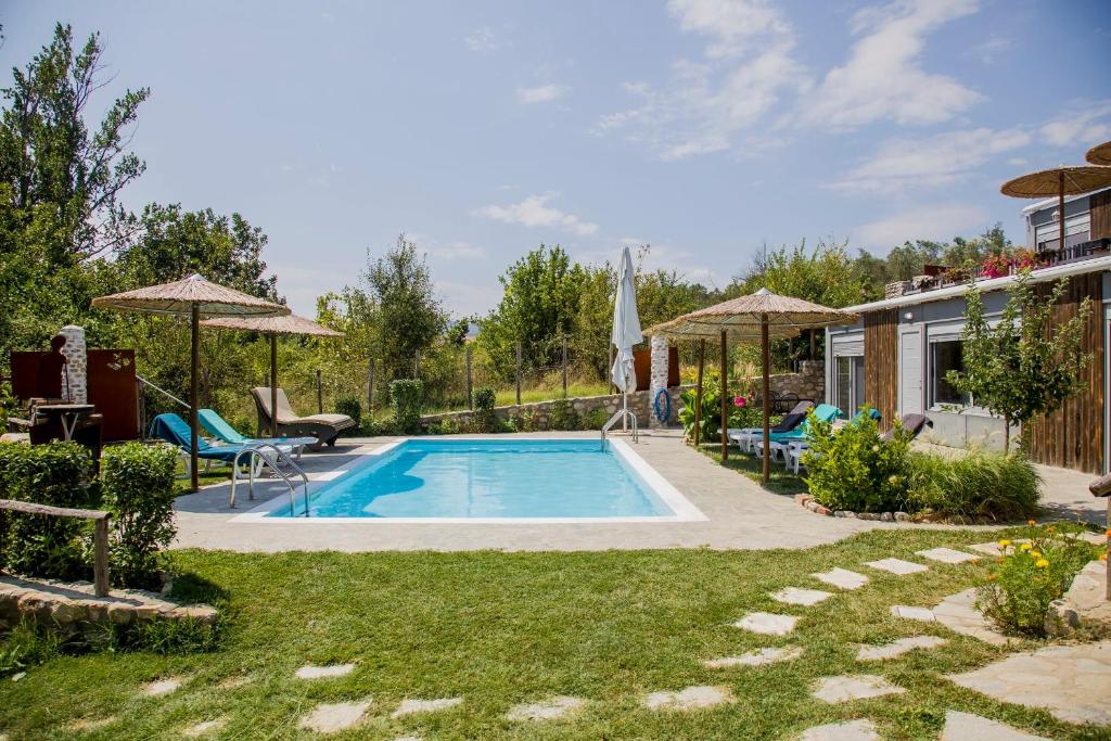 a swimming pool in a yard with chairs and umbrellas at Roxani Aqua Bliss - Serene Garden Getaway in Evkarpía