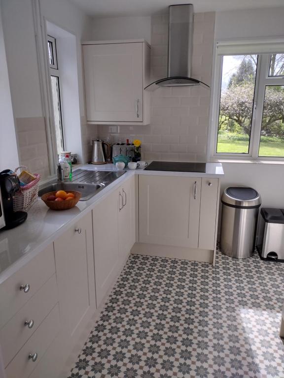 una cucina con armadi bianchi, lavandino e finestra di Robin Hill Cottage ad Amesbury