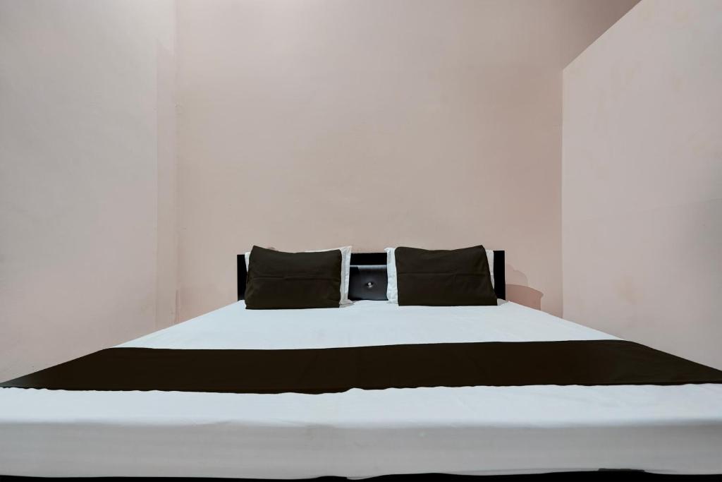 Una cama blanca con almohadas negras encima. en SPOT ON guest house en Bulandshahr