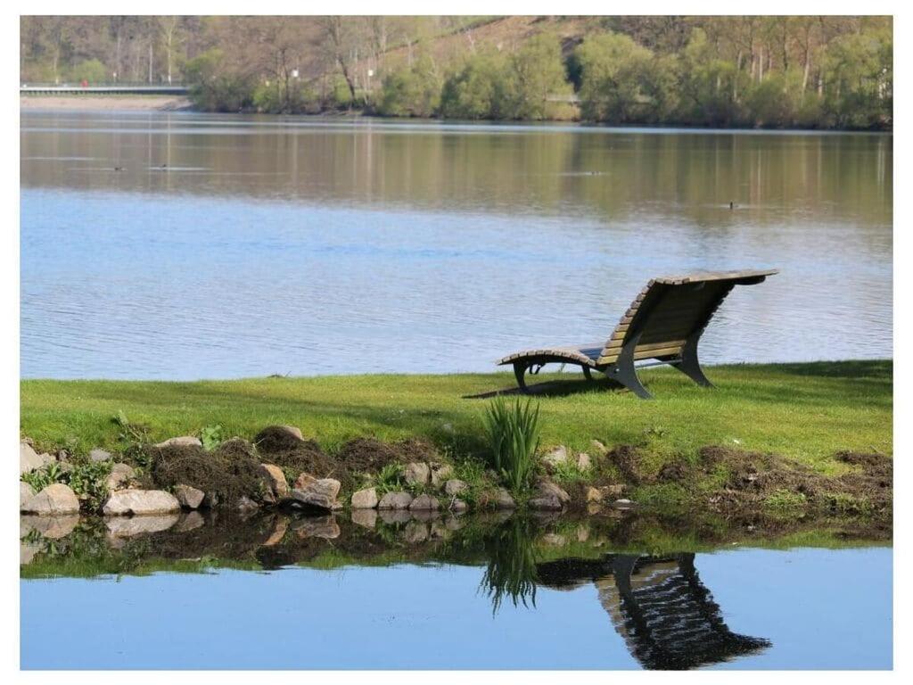 una panchina seduta sull'erba vicino a un lago di Holiday apartment Siuerlänner a Langscheid