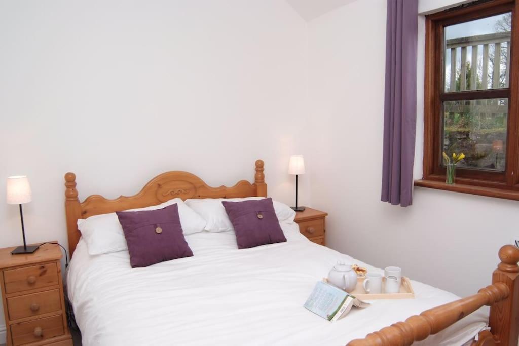 a bedroom with a white bed with purple pillows and a window at Siblyback Cottage in Launceston