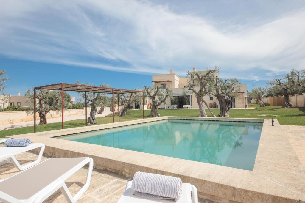 una piscina con 2 sillas blancas y una casa en Casale degli Ulivi by Apulia Hospitality, en Fasano