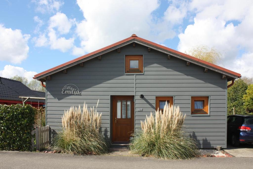 una pequeña casa gris con una puerta marrón en Villa Emilia - Gemütliches kinderfreundliches Blockhaus mit umzäuntem Garten en Sint Annaland