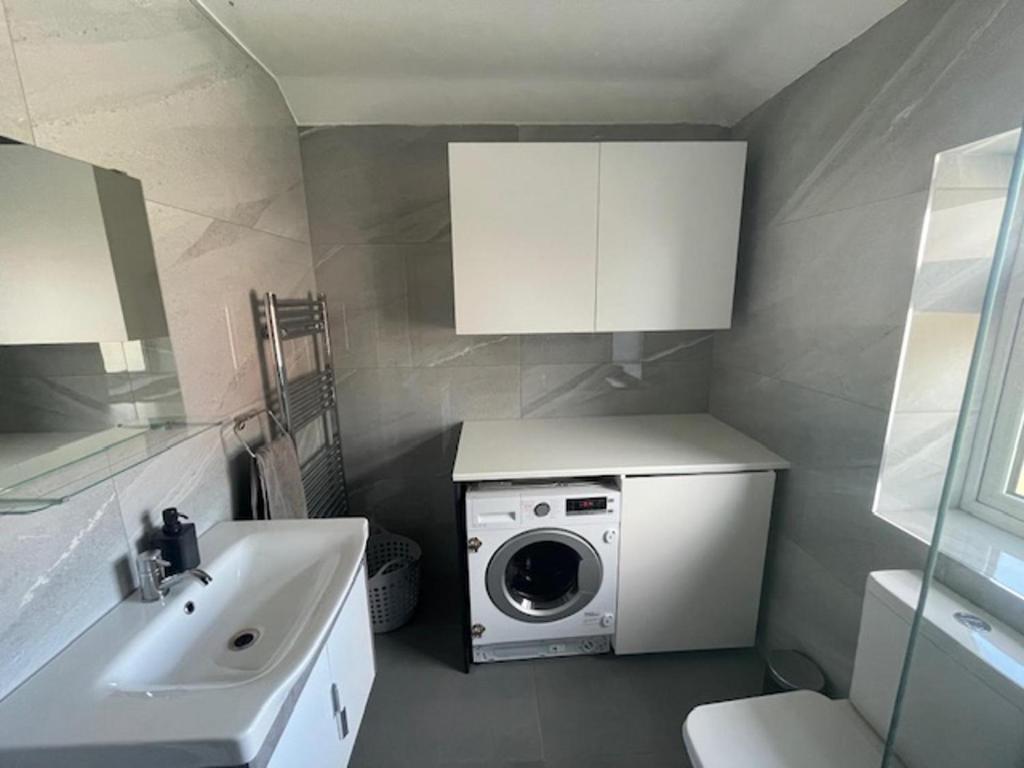 uma casa de banho com uma máquina de lavar roupa e um lavatório em Impeccable Holiday House in London Sleeps four em Londres