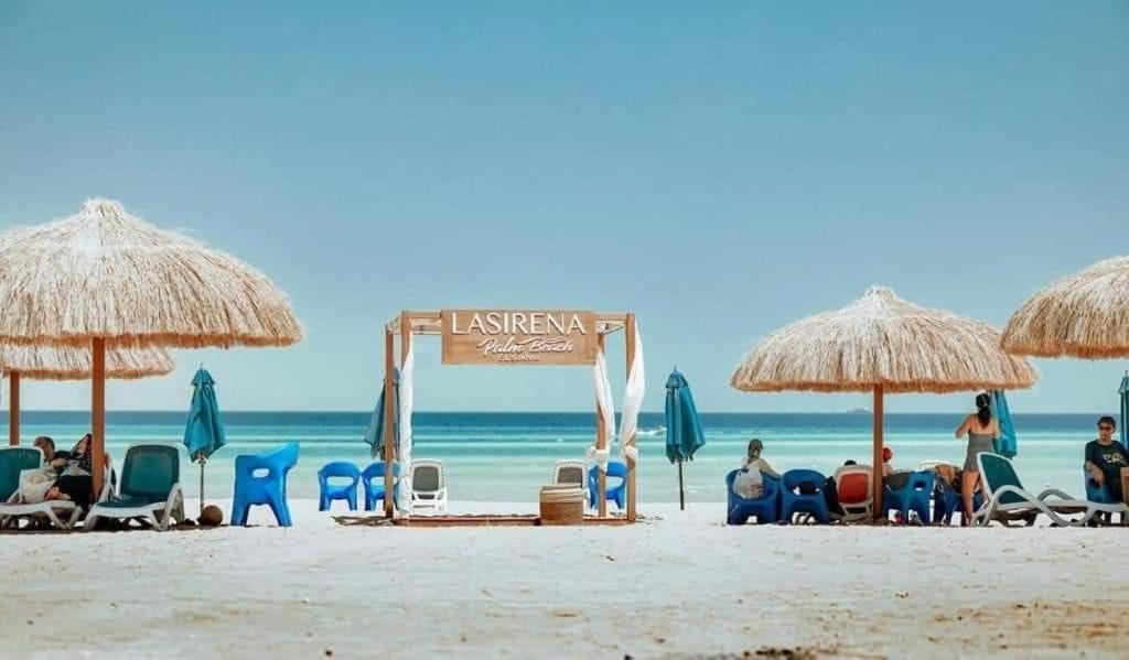 eine Gruppe von Personen am Strand mit Stühlen und Sonnenschirmen in der Unterkunft LASIRENA PALM BEACH RESORT -FAMILY in Ain Suchna