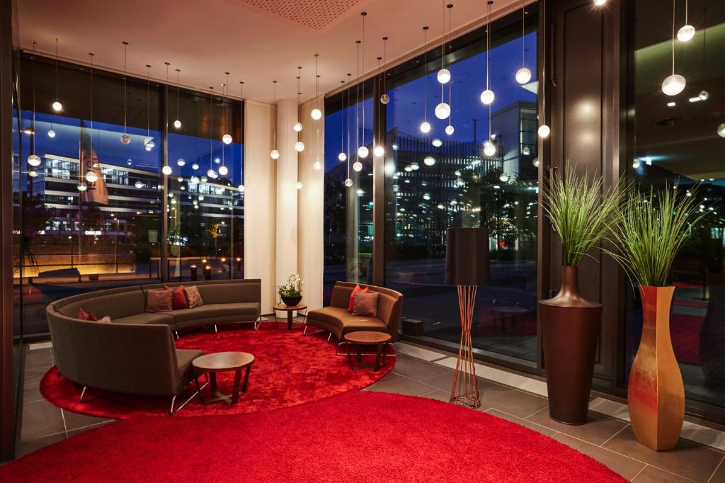 a living room with a red rug and a large window at Steigenberger Hotel Bremen in Bremen
