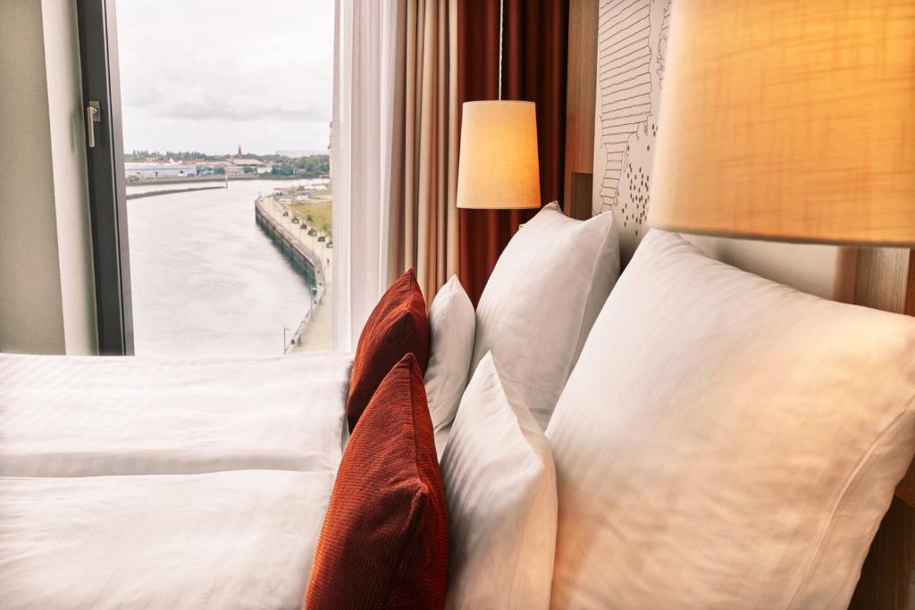 a bedroom with a bed with pillows and a window at Steigenberger Hotel Bremen in Bremen