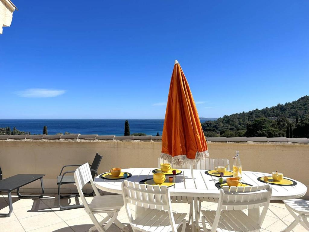 une table et des chaises avec un parasol et l'océan dans l'établissement Appartement 3 pièces 6 pers avec terrasse, clim, piscine privée, parking - FR-1-251-81, au Lavandou