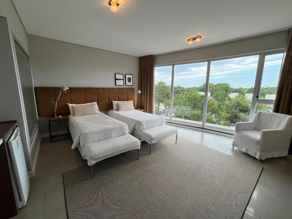 een kamer met 2 bedden, 2 stoelen en een raam bij Hotel Zentiva Pinamar in Pinamar