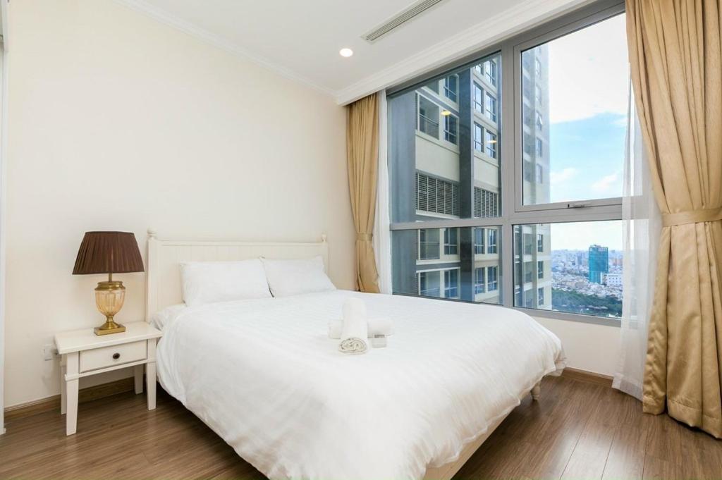 - une chambre avec un lit blanc et une grande fenêtre dans l'établissement Vinhomes Apartment, à Hô-Chi-Minh-Ville