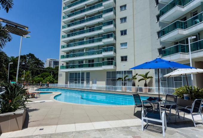 una piscina con sillas, una sombrilla y un edificio en Centro de Convenções Riocentro - O melhor para mais de 2 hóspedes - Shows Rio de Janeiro, RioStay Flat - Cidade do Rock - Jeunesse Arena - Parque Olimpico - Apartamento Duplo Completo, en Río de Janeiro