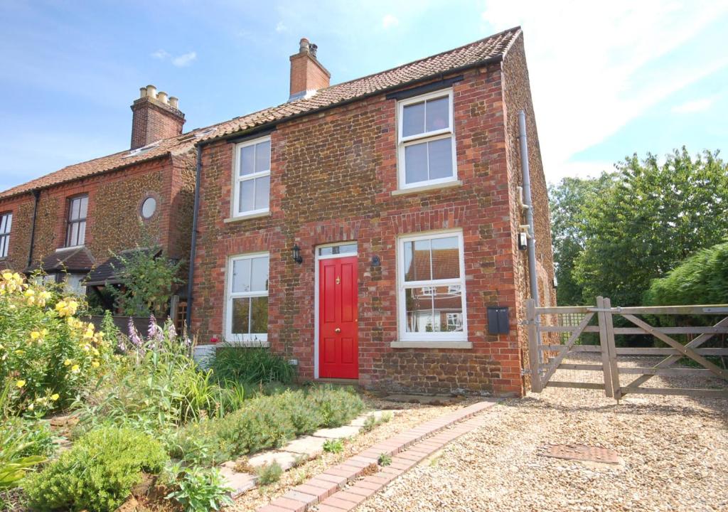 una vieja casa de ladrillo con una puerta roja en Avocet Cottage, en Dersingham