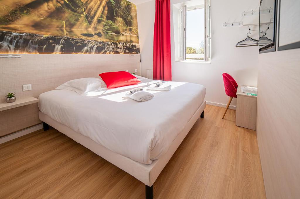 Schlafzimmer mit einem großen weißen Bett und einem roten Kissen in der Unterkunft Hôtel de la Mairie in Saint-Pol-de-Léon