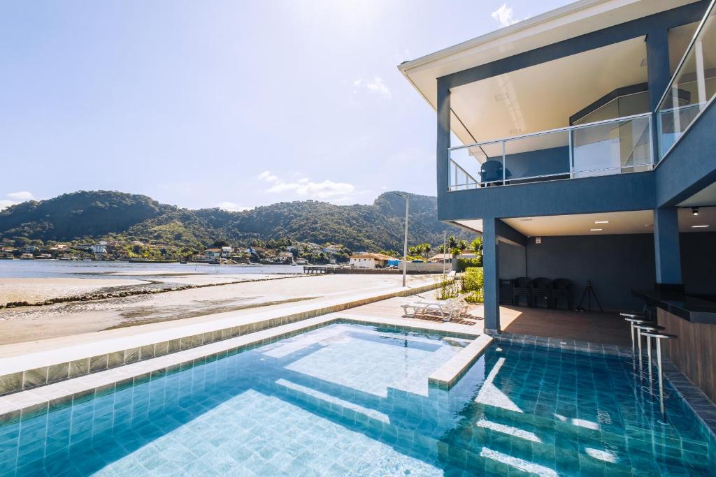 uma casa com piscina ao lado de uma praia em VELINN Angra Sunset Hotel & Villas em Angra dos Reis