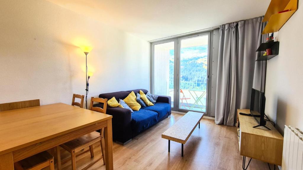 ein Wohnzimmer mit einem blauen Sofa und einem großen Fenster in der Unterkunft Résidence La Petite Ourse - 3 Pièces pour 6 Personnes 83 in Flaine