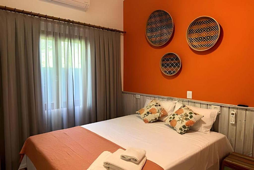 a bedroom with a bed with an orange wall at Vila Saíra, chalé Laranja, 50m da praia in Ilhabela