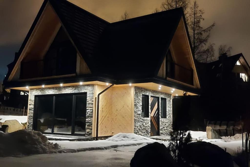Una casa en la nieve con luces encendidas. en tatra homes, en Kościelisko