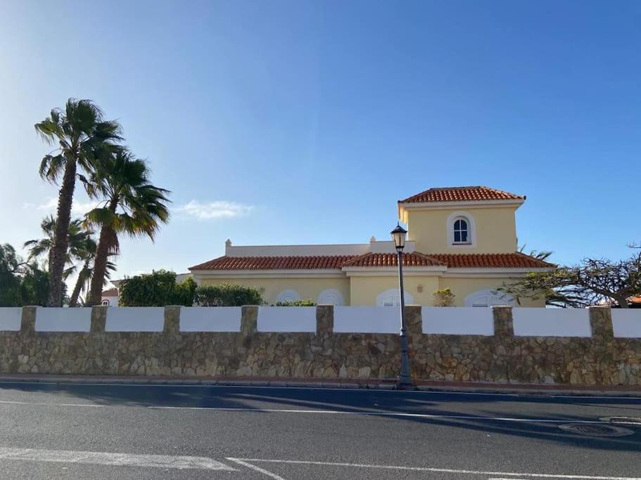 a white house with a fence and palm trees at Oasis Golf Villa in Caleta De Fuste