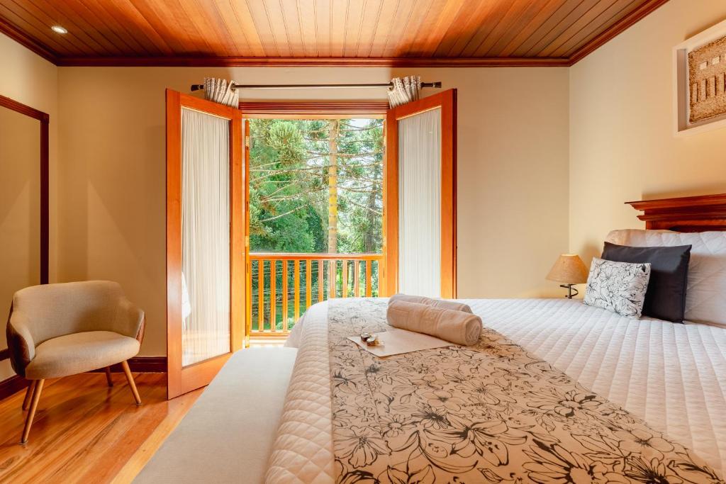 a bedroom with a bed and a window and a chair at Pousada Villa D'Biagy in Campos do Jordão