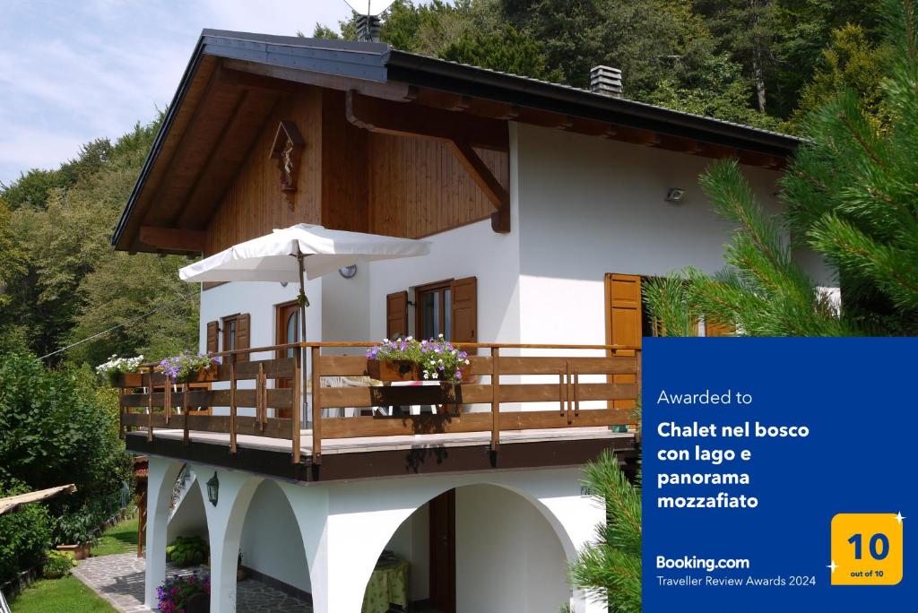 a small house with a balcony with an umbrella at Chalet nel bosco con lago e panorama mozzafiato in Lagolo di Calavino