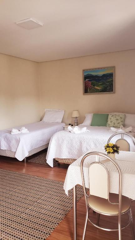 two beds in a room with two chairs at Suítes Bela Joao e Maria in Campos do Jordão