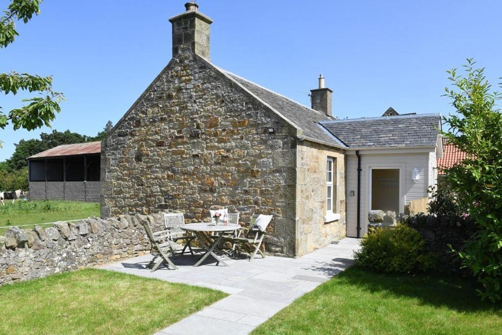 una casa de piedra con una mesa y sillas en el patio en Fordel Cottage, en Dalkeith