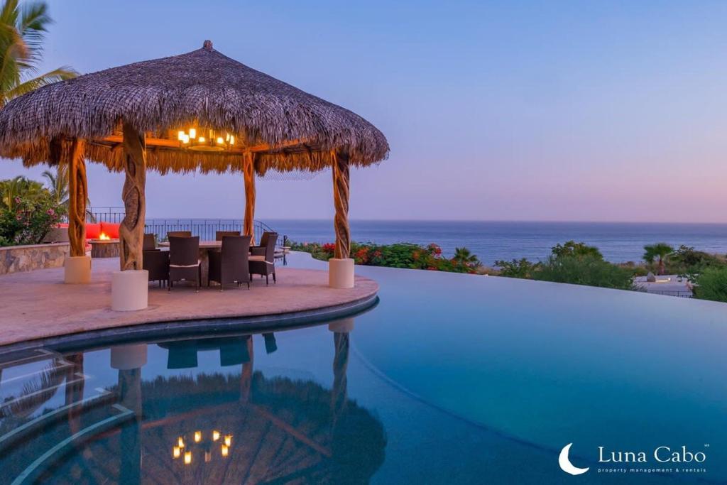 a swimming pool with a umbrella and chairs and the ocean at Firepit Sunsets, Hot Tub Soaks, BBQ, Ocean Views in San José del Cabo
