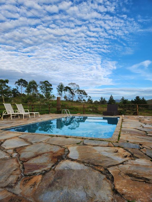 uma piscina com duas cadeiras e um céu azul em Chales Sitio dos Ventos em Lavras Novas