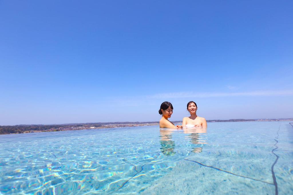 dos mujeres de pie en el agua en la playa en Ooedo Onsen Monogatari Premium Yamashitaya en Kaga