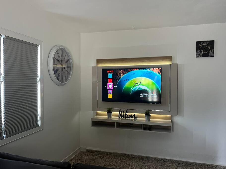 a flat screen tv on a wall with a clock at Villa Orquídea 4 in Humacao
