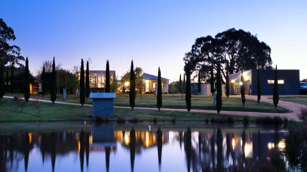 a park with a pond with trees and a building at The Welcome Paddock in Hepburn