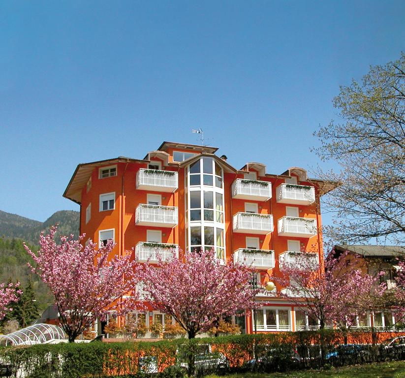 um edifício laranja com árvores floridas à sua frente em Nature Bio Hotel Elite em Levico Terme