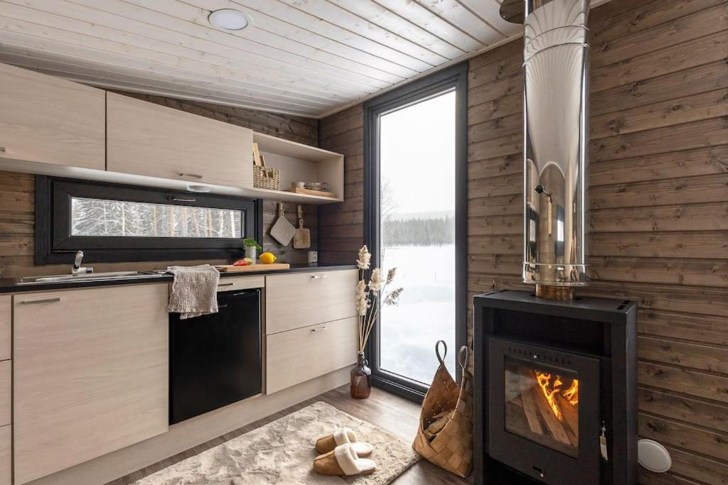 a kitchen with a fireplace and a stove at KARPALO Lapland Riverside Cabin with Sauna Fireplace BBQ WiFi Ski Ylläs PetsOK in Äkäslompolo