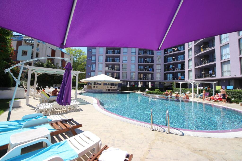 una piscina con tumbonas y una sombrilla púrpura en Menada Rainbow Apartments, en Sunny Beach