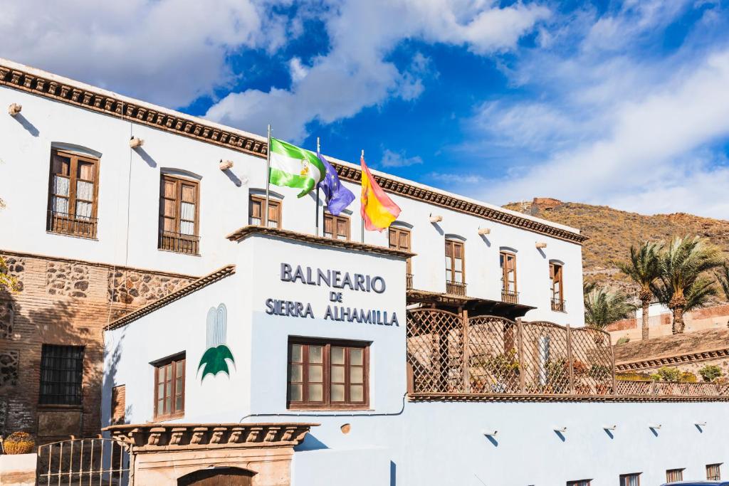 Un bâtiment blanc avec des drapeaux au-dessus dans l'établissement Hotel Balneario De Sierra Alhamilla, à Pechina