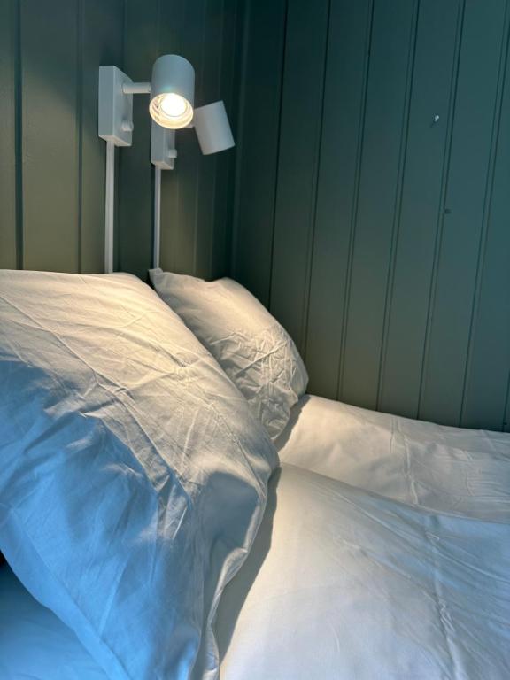 un letto con lenzuola bianche e una luce su un muro di KM Rentals - Lillestrøm City - Private Rooms in Shared Apartment a Lillestrøm