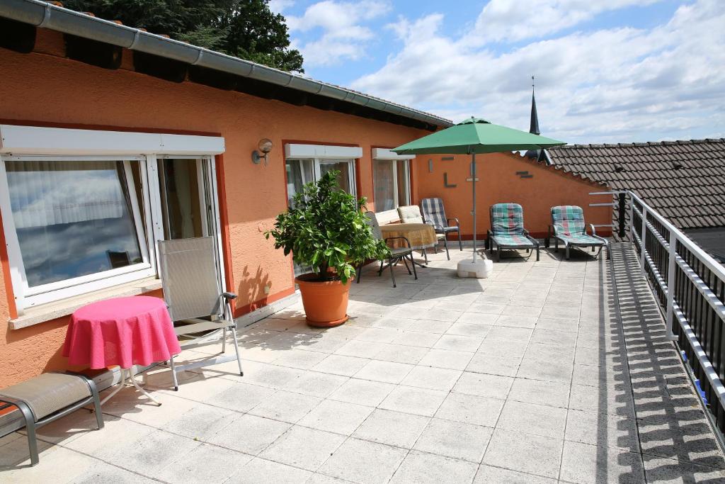 een patio met stoelen, een tafel en een parasol bij Pension Weinberg mit Landhaus Nizza in Gleisweiler
