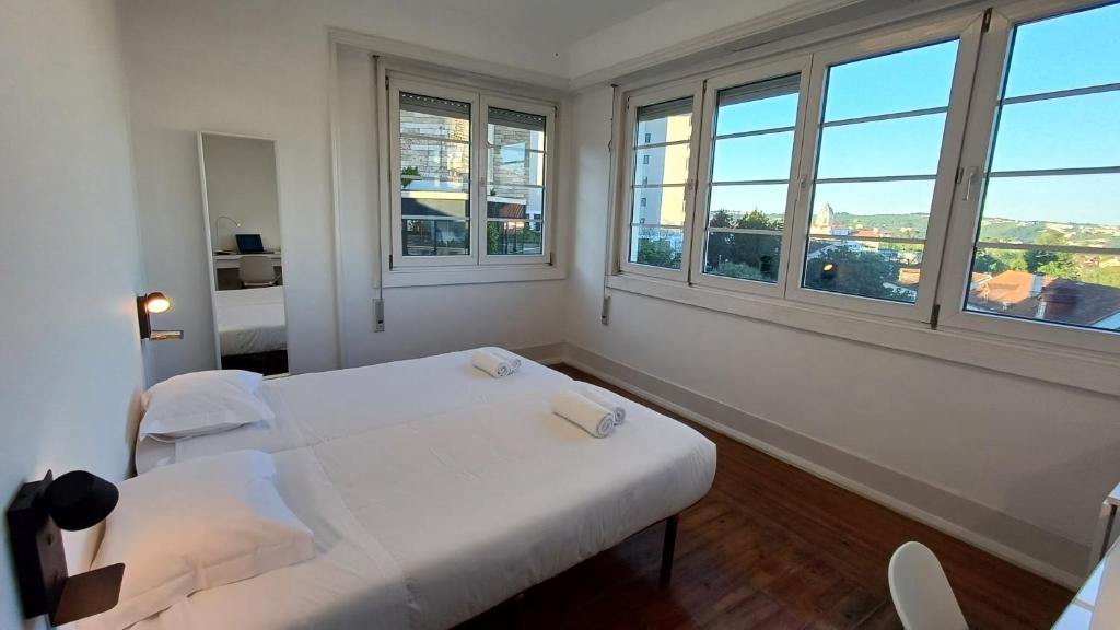 um quarto com uma cama branca e 2 janelas em HI Coimbra - Pousada de Juventude em Coimbra