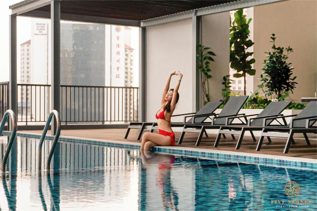 a woman in a bikini sitting next to a swimming pool at Chambers Kuala Lumpur by Five Senses in Kuala Lumpur
