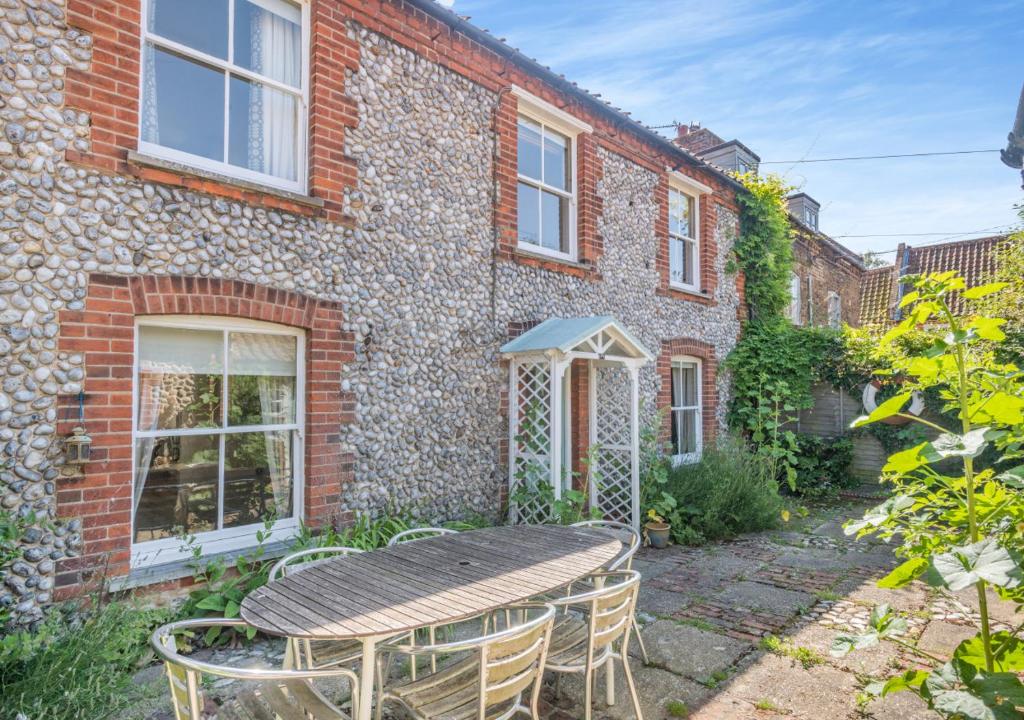 a patio with a table and chairs in front of a brick building at Point Cottage in Blakeney