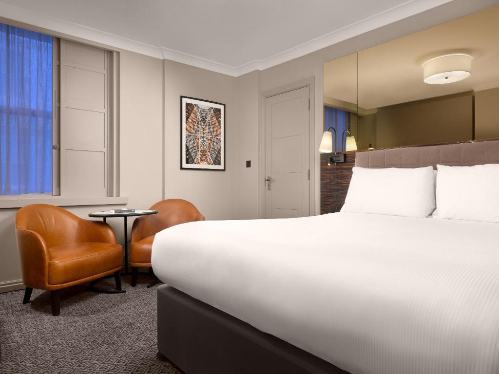 a hotel room with a large bed and a chair at Strand Palace in London
