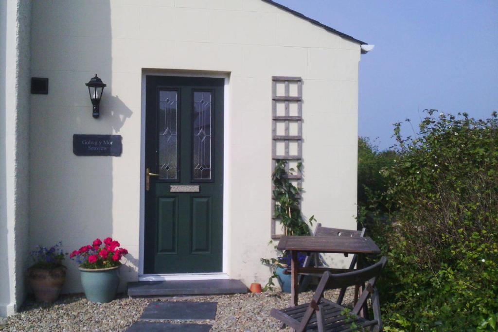 eine grüne Tür auf einem weißen Haus mit einer Bank in der Unterkunft Seaview at Merton Hall Dinas Cross in Dinas